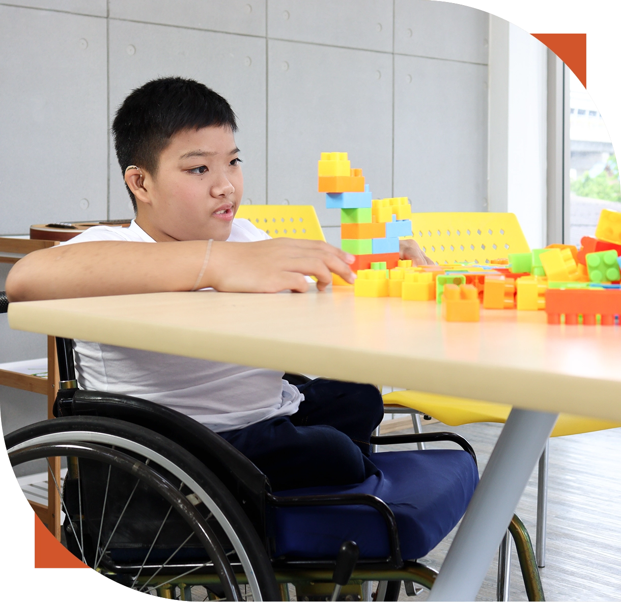 Child in wheelchair playing with colorful blocks.